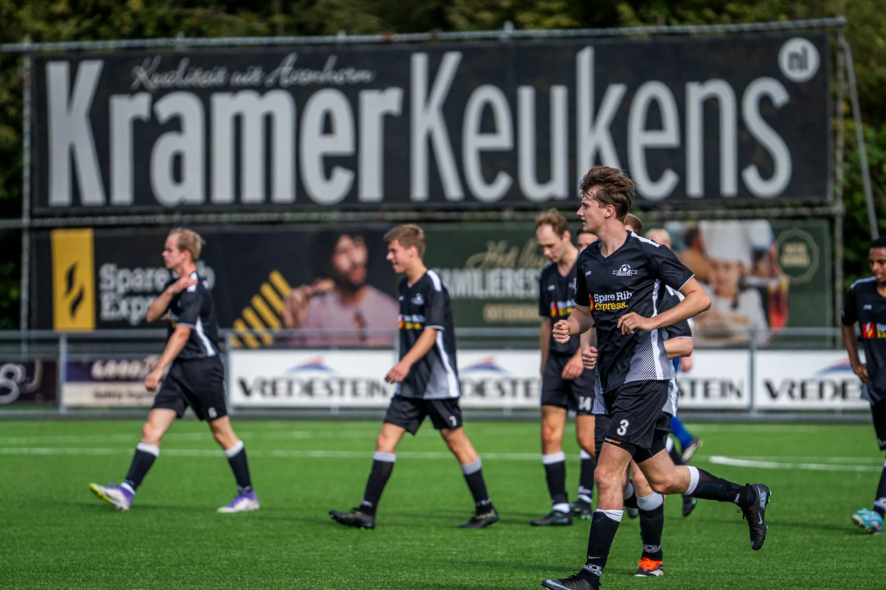Spelers van Kwiek '78 lopen terug voor het grote reclamebord van Kramer Keukens langs het veld