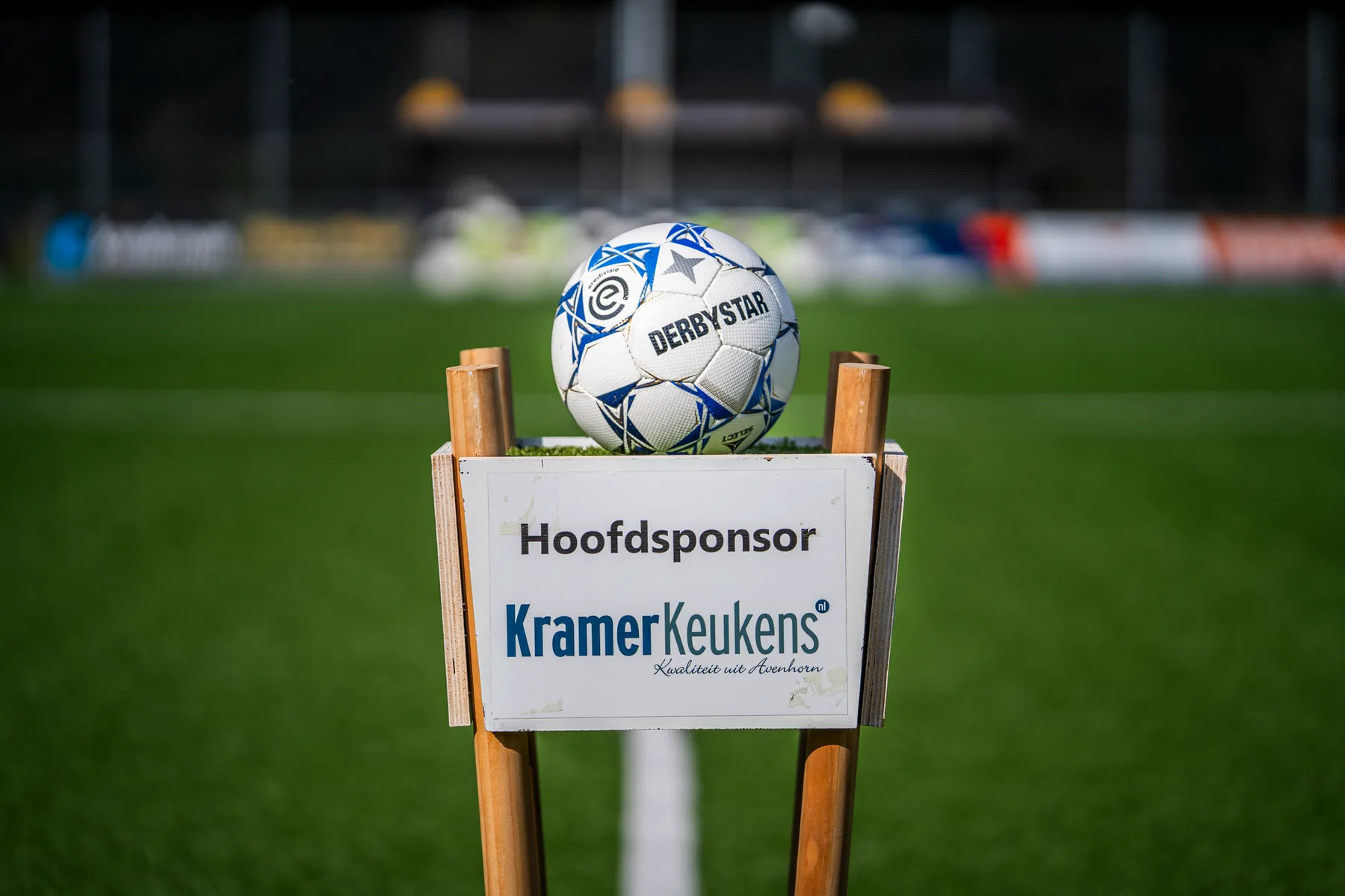 De wedstrijdbal op een houten standaard met het bordje van hoofdsponsor Kramer Keukens